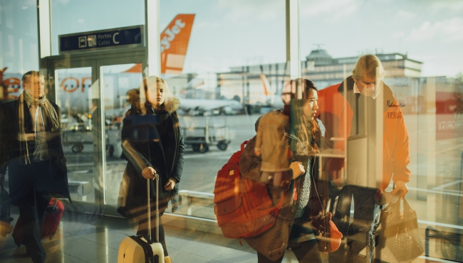 Passengers wandering aimlessly through airport departures with an EasyJet aircraft in the background
