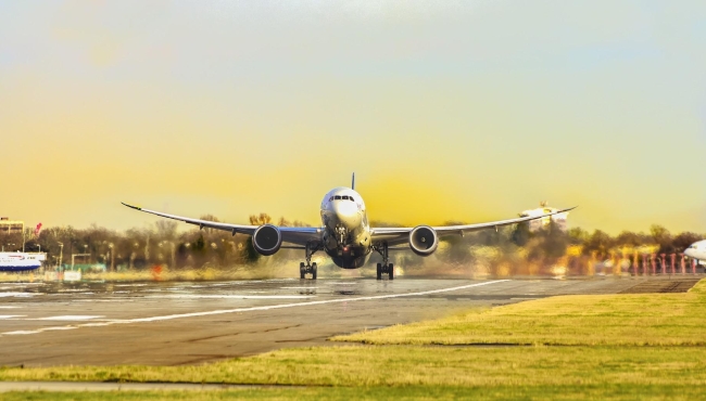 A Boeing 787 Dreamliner on takeoff from an airport with grass, runway and sky in the background