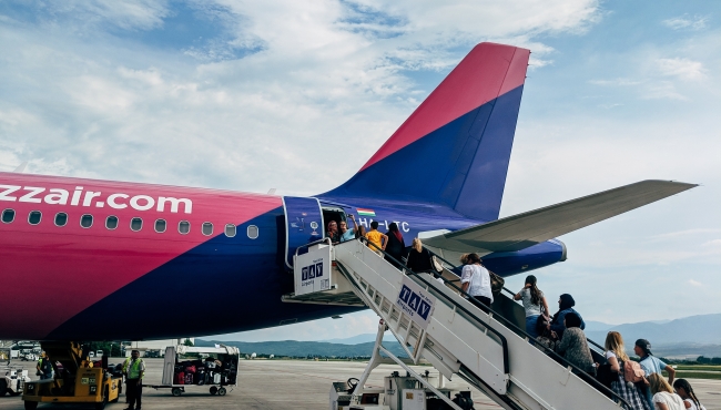 passengers board a wizz air airbus a320 aircraft using a set of steps with mountains and a blue sky in the background
