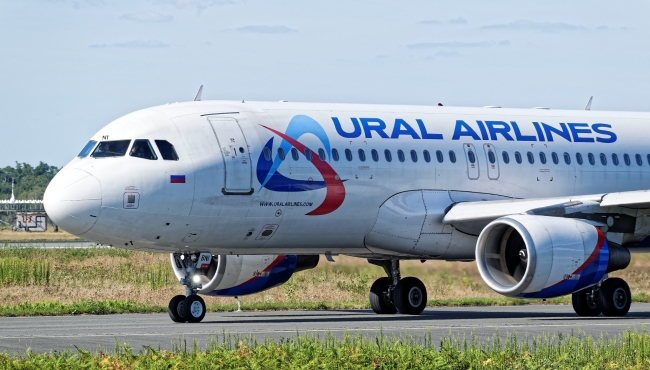 A Ural airlines Airbus A320 passenger jet on the ground at an airport with grass and sky in the background