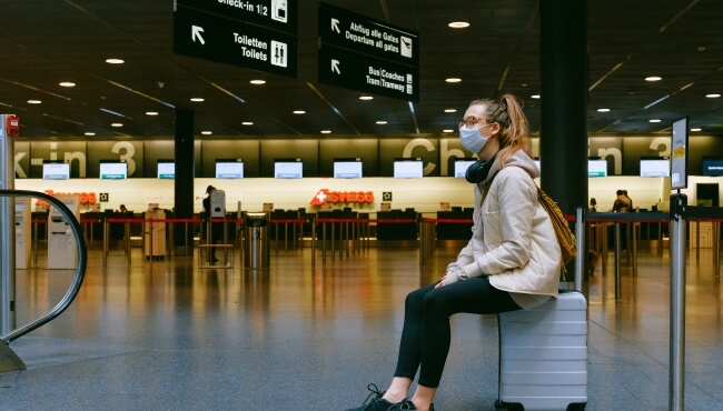 image of a woman sat on her suitcase waiting at an airport