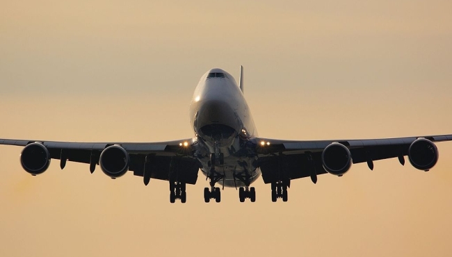 A Boeing 747 jumbo jet landing with wheels down with a sunset sky in the background