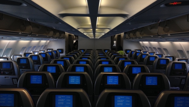 An interiorview of a widebody aircraft cabin, with rows of aircraft seats and in flight entertainment screens